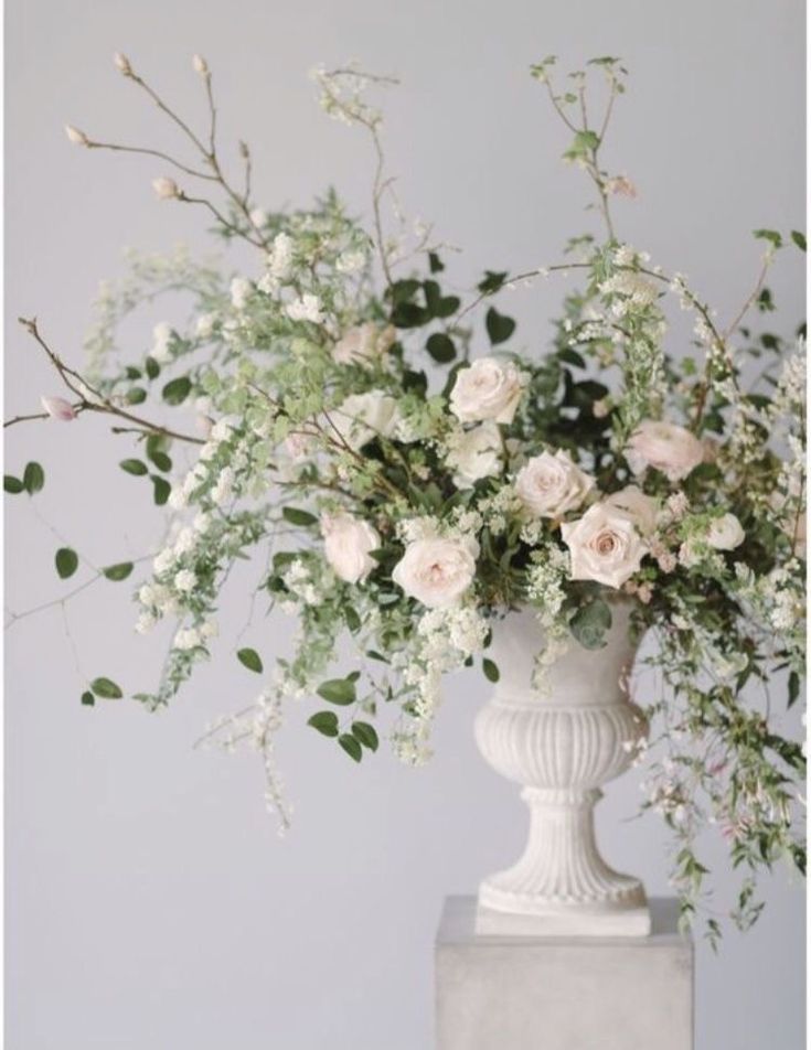 a white vase filled with lots of flowers on top of a marble block stand next to a wall