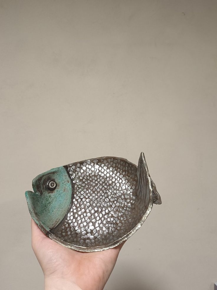 a hand holding a small metal fish dish