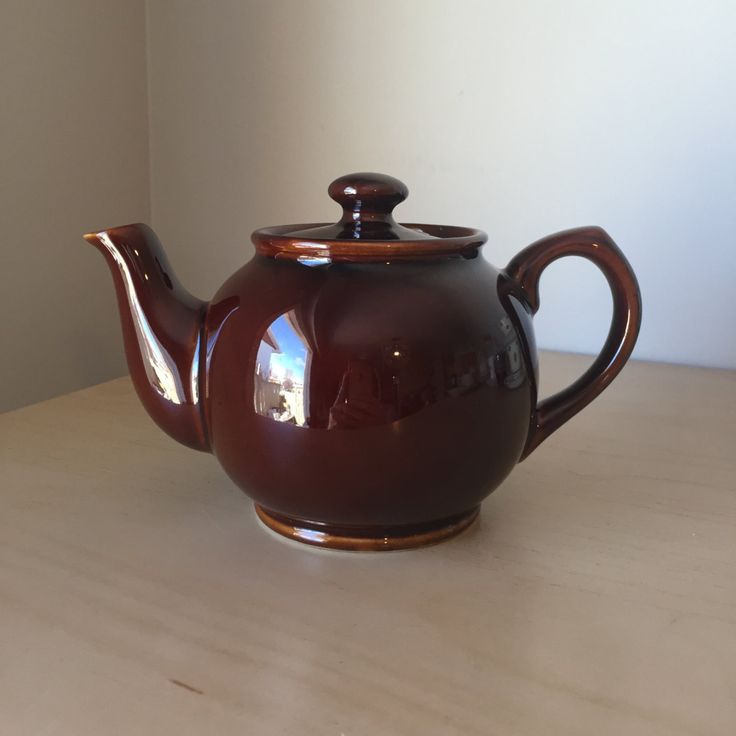 a brown teapot sitting on top of a wooden table next to a white wall