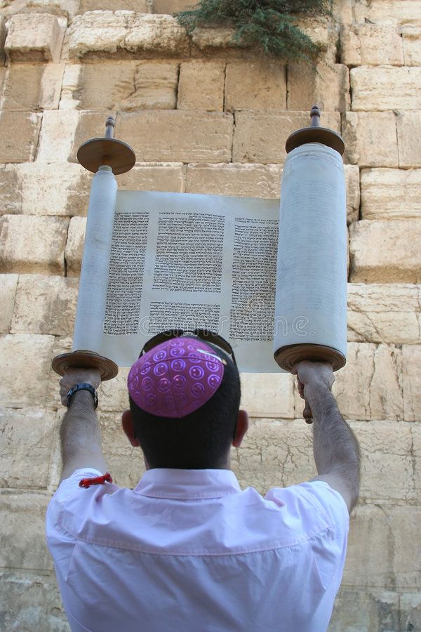 a man is holding up two large objects in front of a stone wall with writing on it