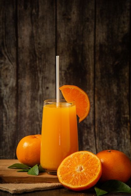 an orange juice in a glass surrounded by sliced oranges on a wooden table, with a straw sticking out of the top