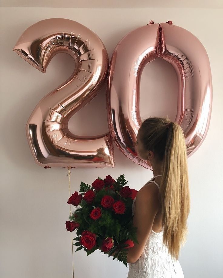 a woman in a white dress holding a bouquet of red roses next to the number 20 balloon