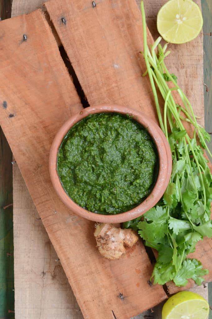 a wooden cutting board topped with a bowl of green pesto next to lemons and cilantro