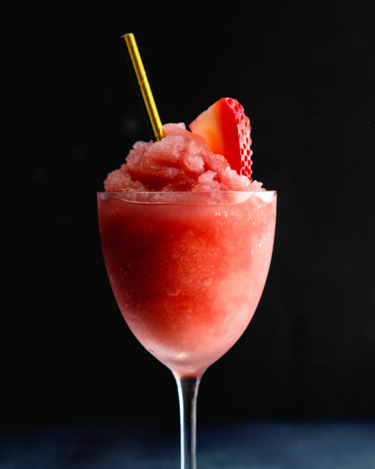 a pink drink with strawberries in it on a blue tablecloth next to a black background