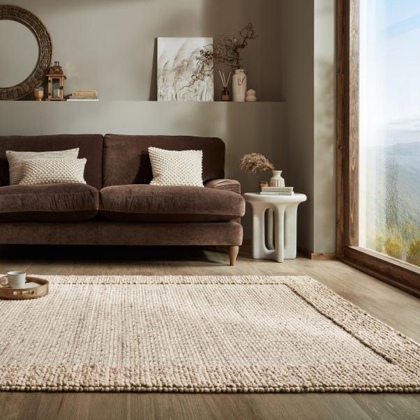 a living room with a brown couch and white rug on the floor next to a window