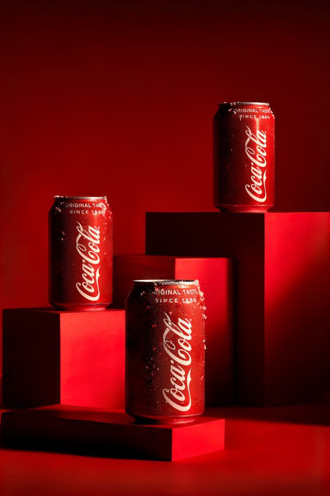 three cans of coca - cola are sitting on red blocks in front of a red background