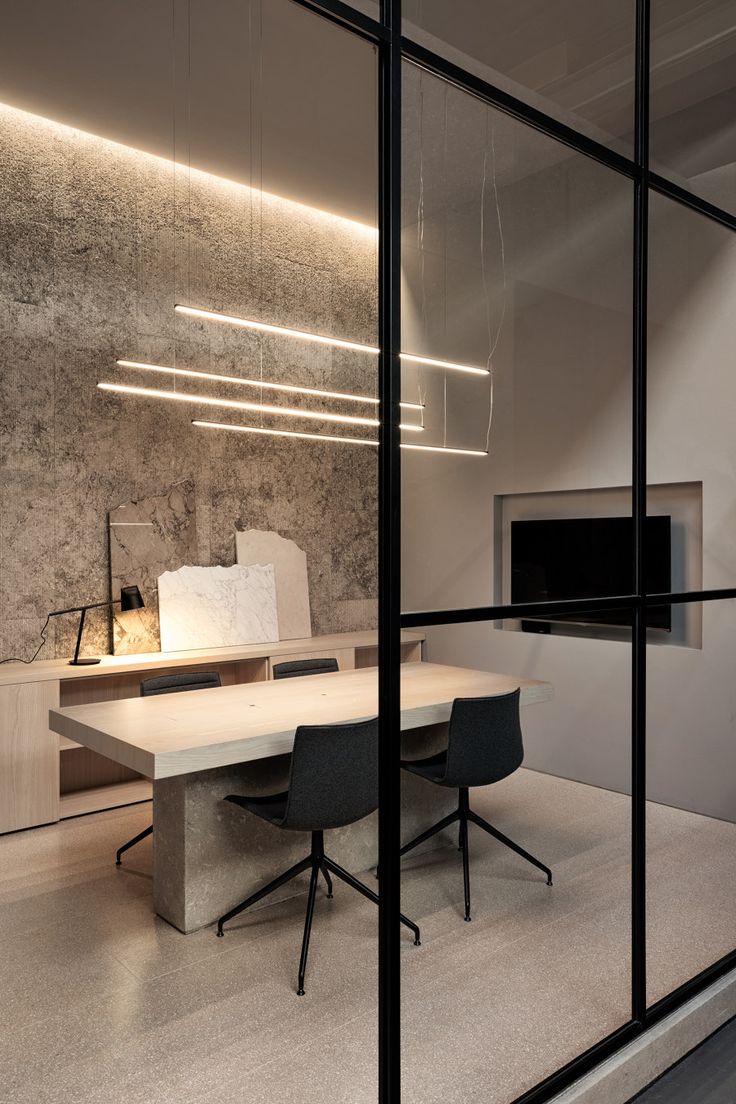 an office with glass walls and desks in front of the wall is lit by lights