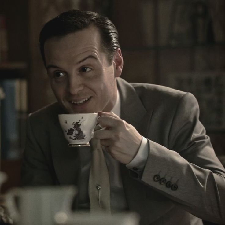 a man in a suit holding a coffee cup and looking at the camera with his mouth wide open