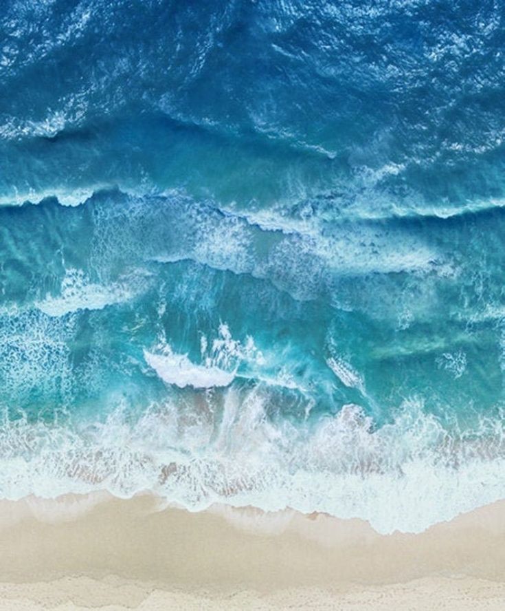 an aerial view of the ocean and beach with waves crashing on it's shore