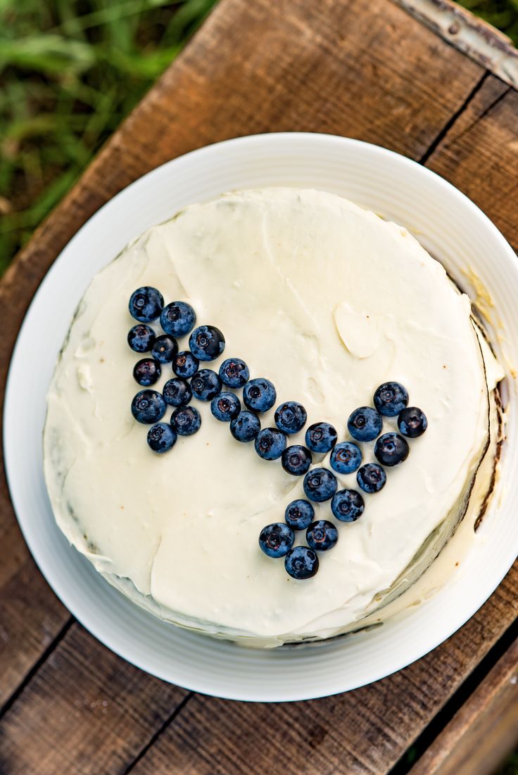 a white cake with blueberries on it sitting on top of a wooden table in the grass