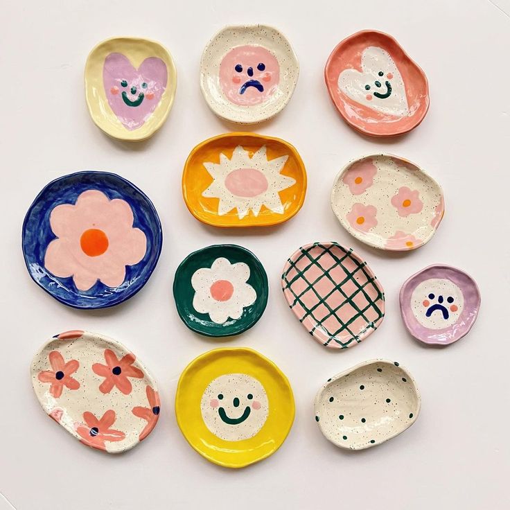 nine plates with different designs on them sitting on a white surface, one has a smiley face and the other has a flower