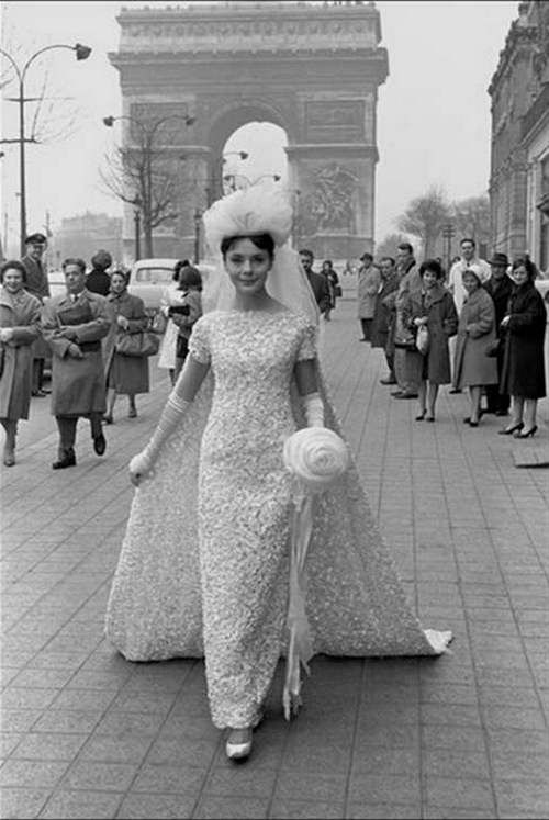 an old black and white photo of a woman in a wedding dress walking down the street