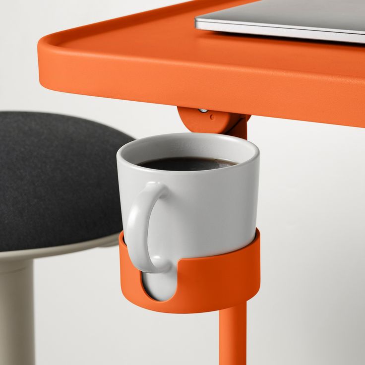 a cup of coffee sitting on top of a table next to an orange desk chair