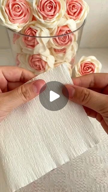 two hands holding a piece of white paper with pink roses in the vase behind them