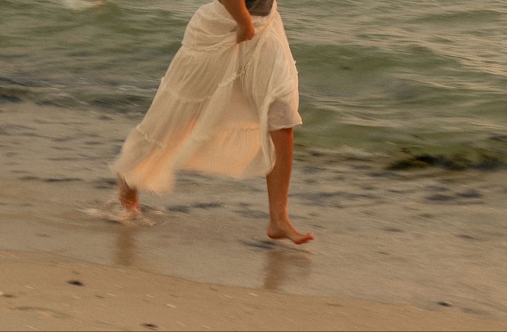 a woman is walking on the beach with an umbrella over her head and holding a cell phone to her ear