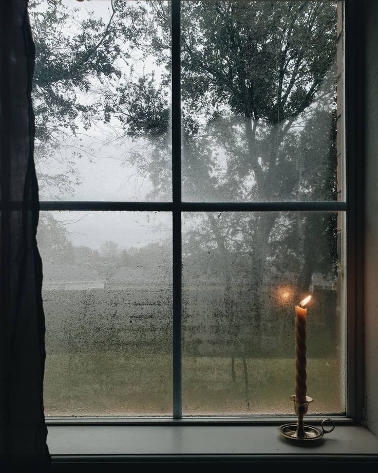 a candle sitting on top of a window sill in front of a foggy field