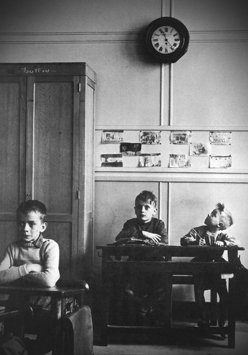 black and white photograph of three children sitting at desks in front of a clock