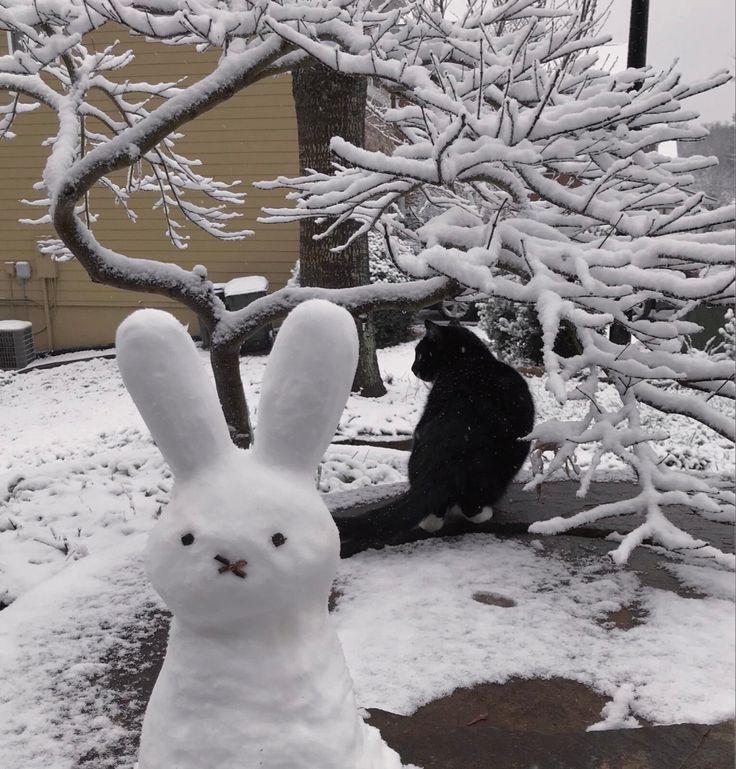 a white rabbit statue sitting next to a black cat on top of snow covered ground