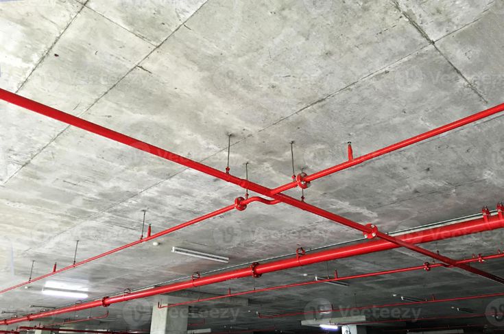 an empty parking garage with red piping on the ceiling