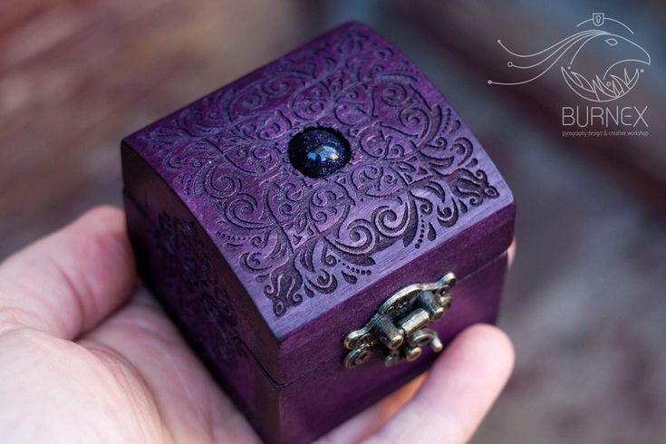 a hand holding a purple wooden box with an intricate design on it