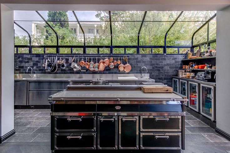 an open kitchen with stainless steel appliances and black counter tops, along with lots of hanging utensils