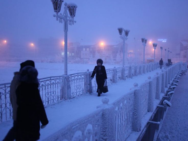 two people walking on a bridge in the snow at night with street lights lit up behind them