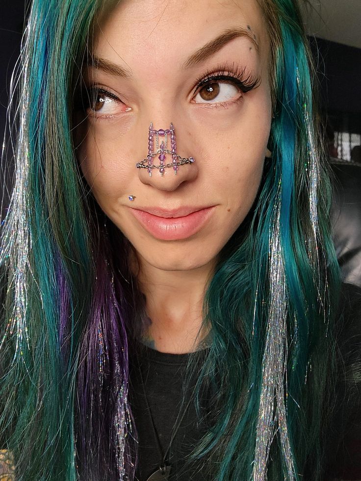 a woman with green and purple hair has her nose piercings in the shape of an m