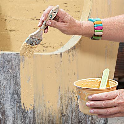 a person painting a wooden chair with a paintbrush and a cup filled with yellow liquid