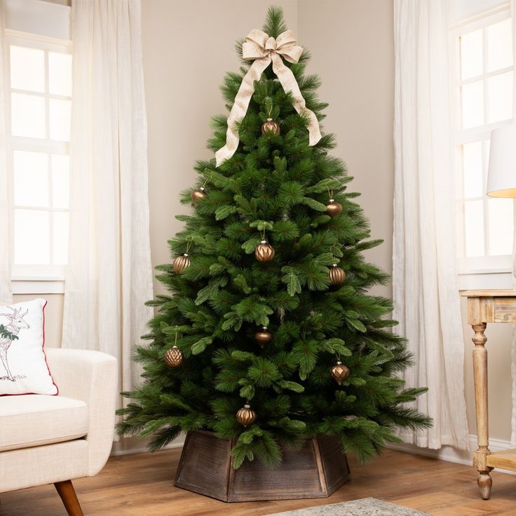 a small christmas tree with gold ornaments and a bow on top in a living room