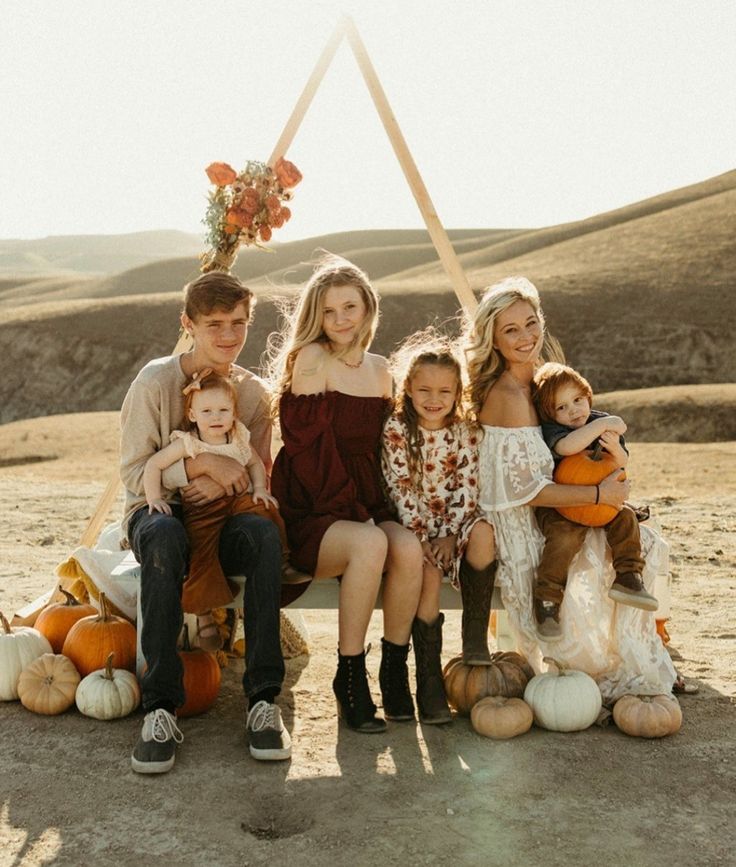 a group of people sitting on top of a bench with pumpkins in front of them