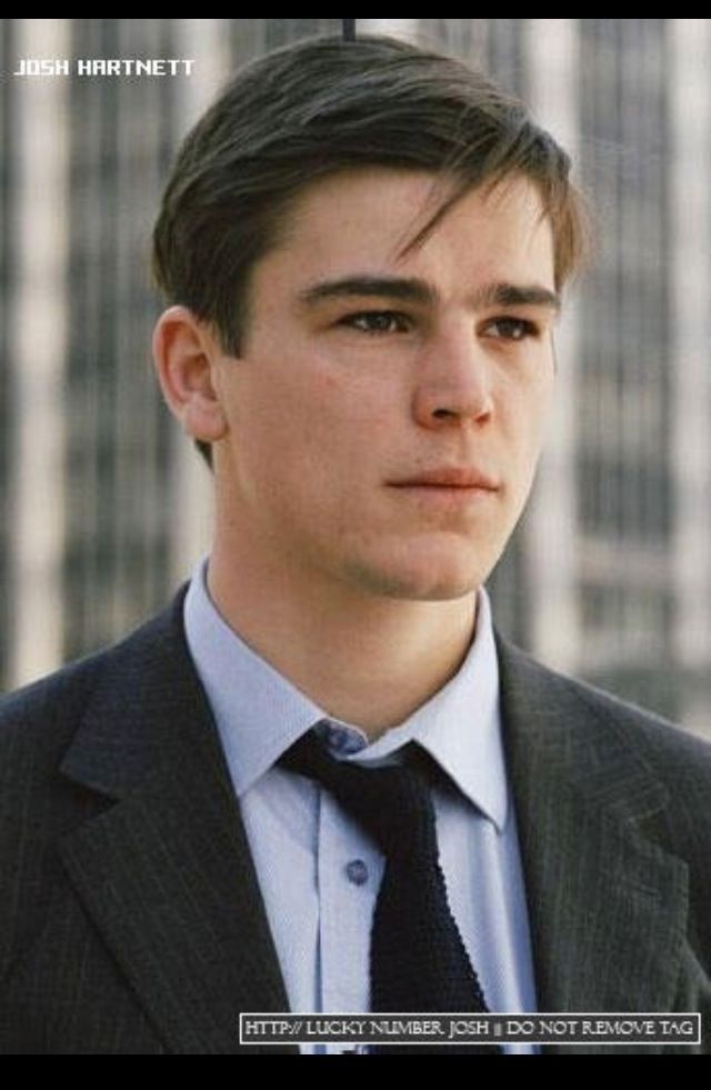 a young man in a suit and tie looking at the camera with buildings in the background