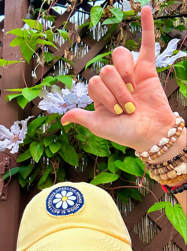 a person with their hand up in front of a fence and some flowers on the other side