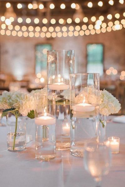 the centerpieces are filled with white flowers and lit candles in glass vases