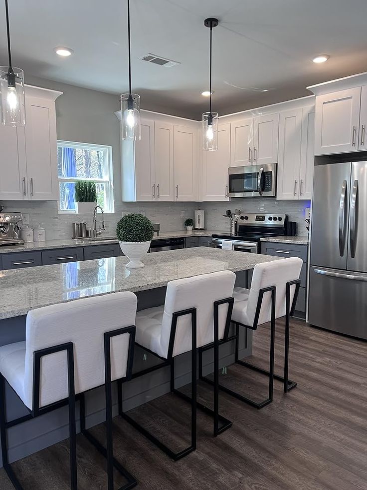 a kitchen with an island and white chairs in front of the counter top, along with stainless steel appliances