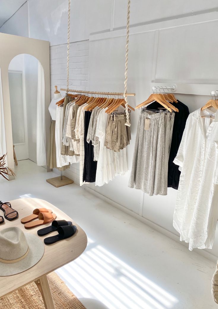 clothes are hanging on the rack in front of a table with shoes and hats sitting on it