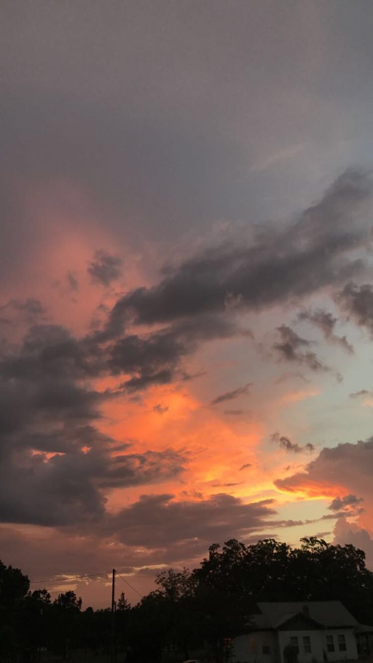 the sun is setting behind some clouds in the sky with houses and trees around it