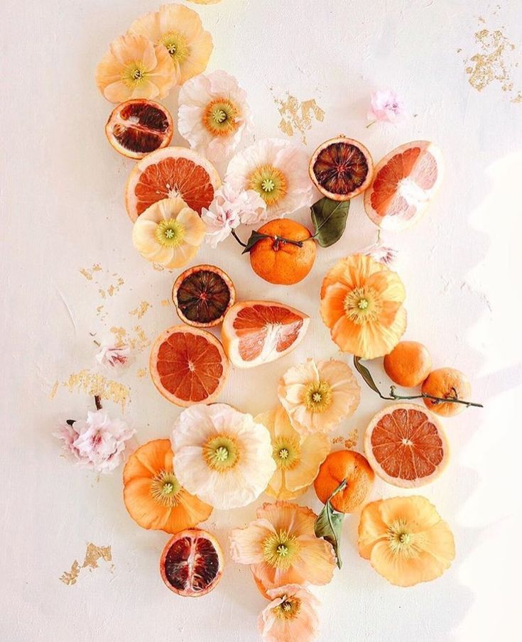 an arrangement of oranges and flowers on a white surface