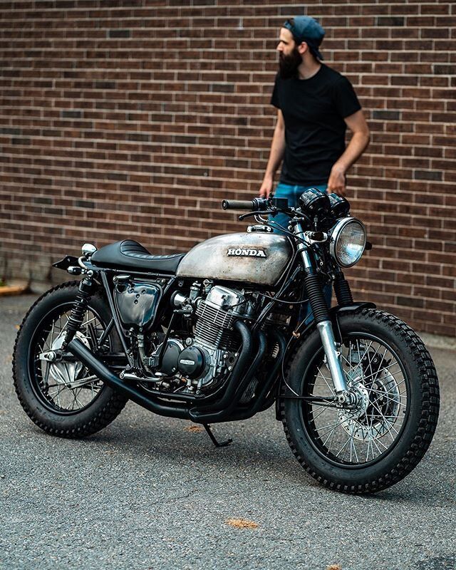 a man standing next to a parked motorcycle in front of a brick wall and wearing a bandana