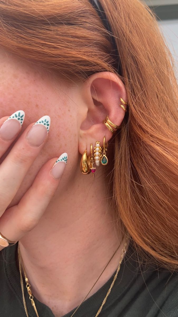 a woman with red hair wearing gold and white nail polish holding her hands to her face