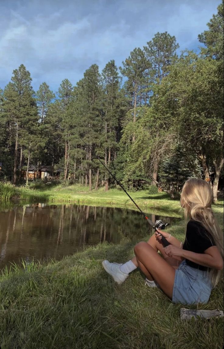 a woman sitting on the grass with a fishing rod