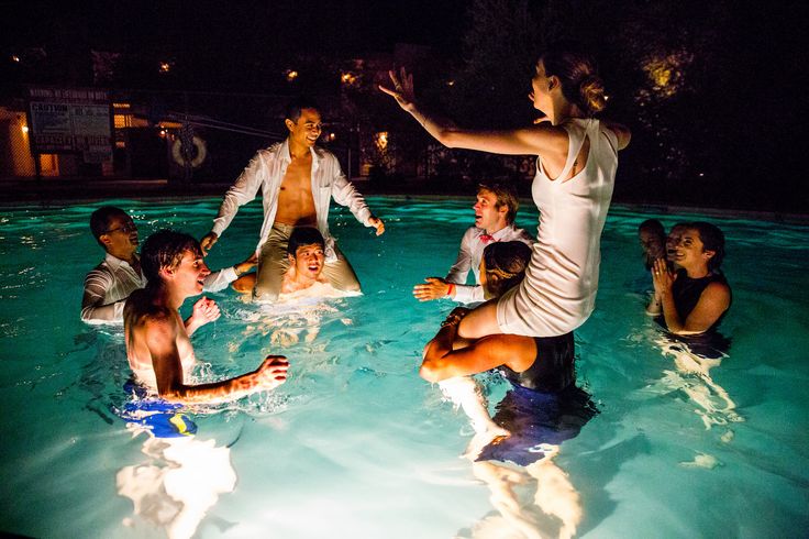 a group of people are in the pool at night, with one person holding out his hand