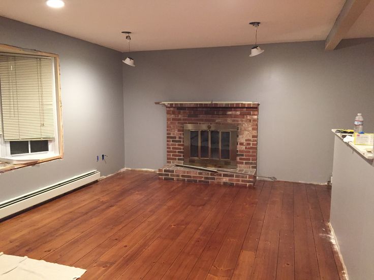 an empty living room with hard wood flooring and a brick fireplace in the corner