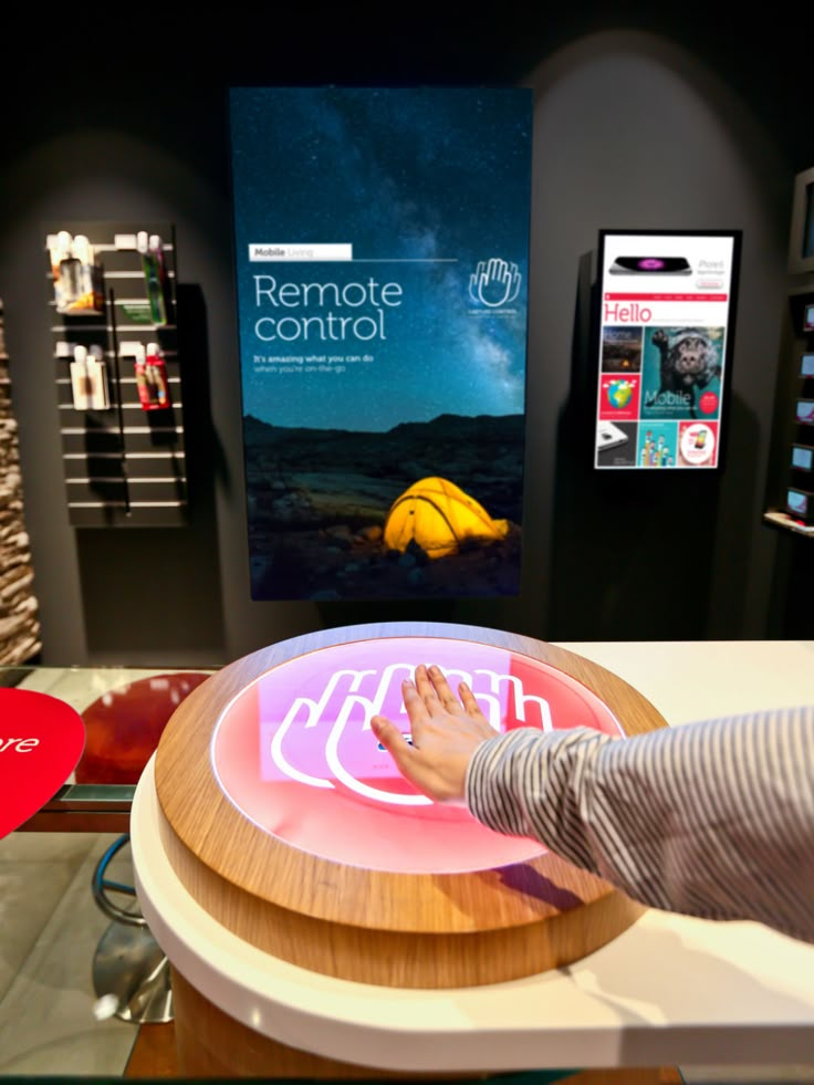 a person standing at a table with a remote control in front of them and an advertisement on the wall behind it