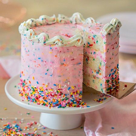 a pink cake with white frosting and sprinkles on a plate next to a fork