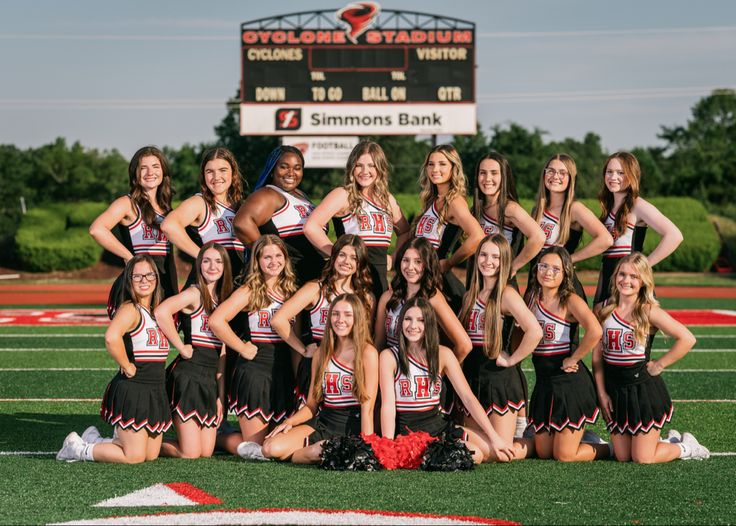 a group of cheerleaders posing for a photo on the field in front of a scoreboard