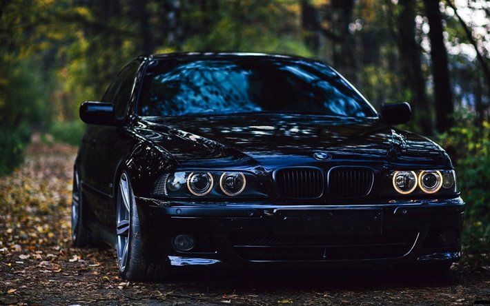 a black car parked on the side of a road in front of trees and leaves