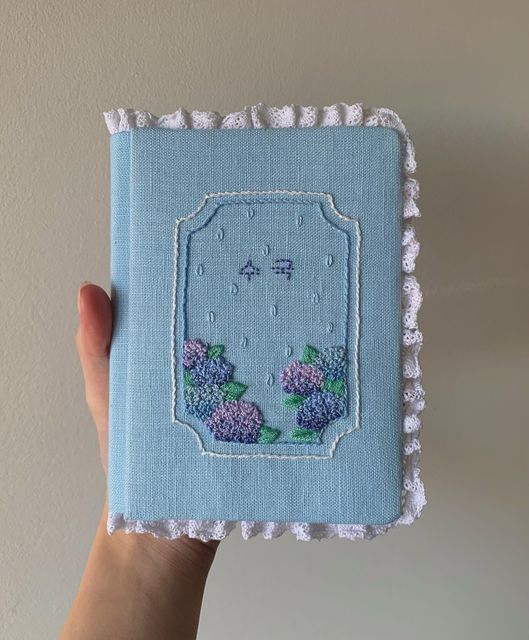 a hand holding an embroidered book with flowers on it