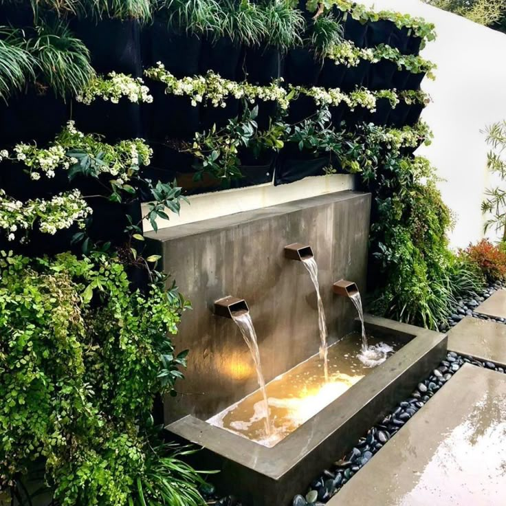 an outdoor fountain with water flowing from it's sides and surrounded by greenery