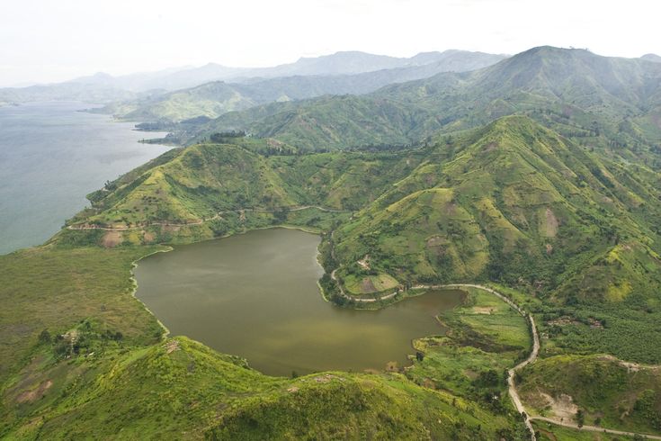 an aerial view of a lake surrounded by lush green hills and mountains in the distance