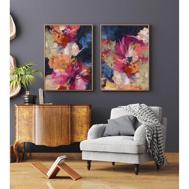 two paintings hang on the wall next to a chair and sideboard in a living room